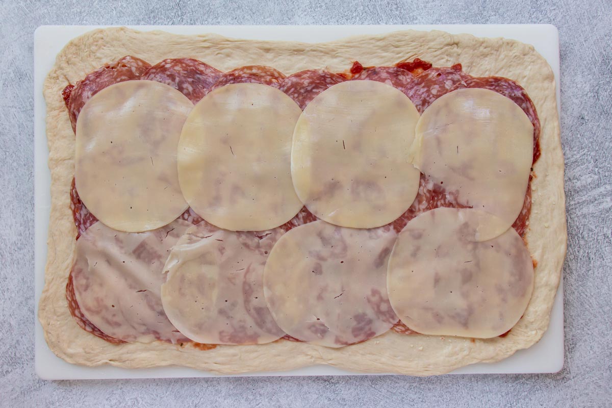 Sliced provolone cheese arranged in rows on top of a rectangular pizza dough.