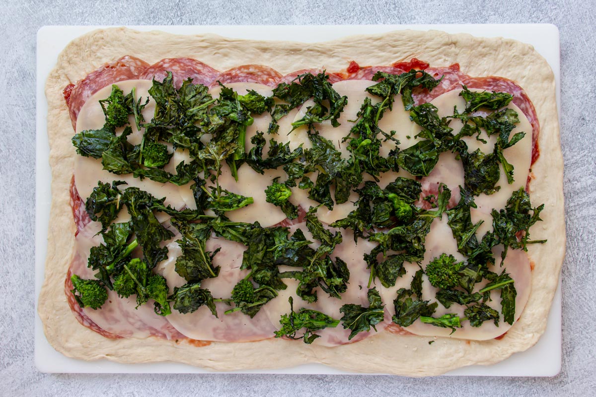 Roasted rapini (broccoli rabe) sprinkled over the top of a cheese covered pizza dough.
