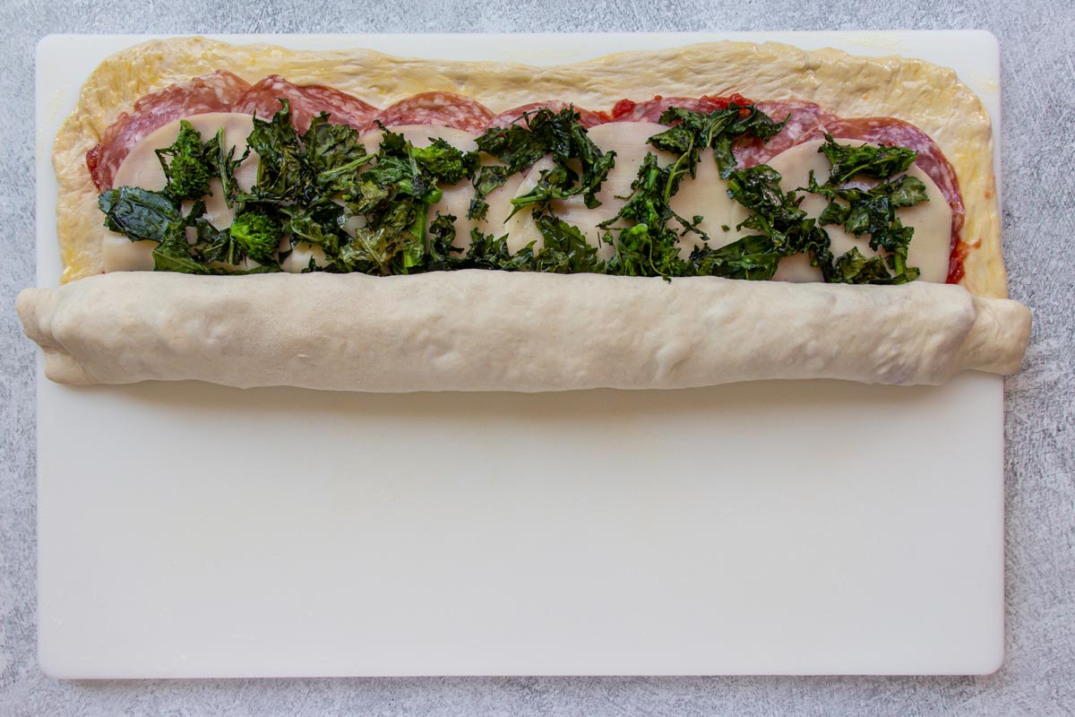 Rolling up a stromboli pizza into a long cylinder on a white board.