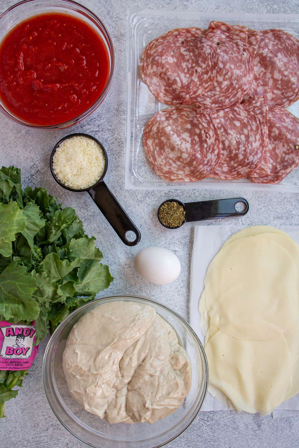 Ingredients for stromboli including soppressata salami, rapini, provolone, pizza, dough, and an egg.