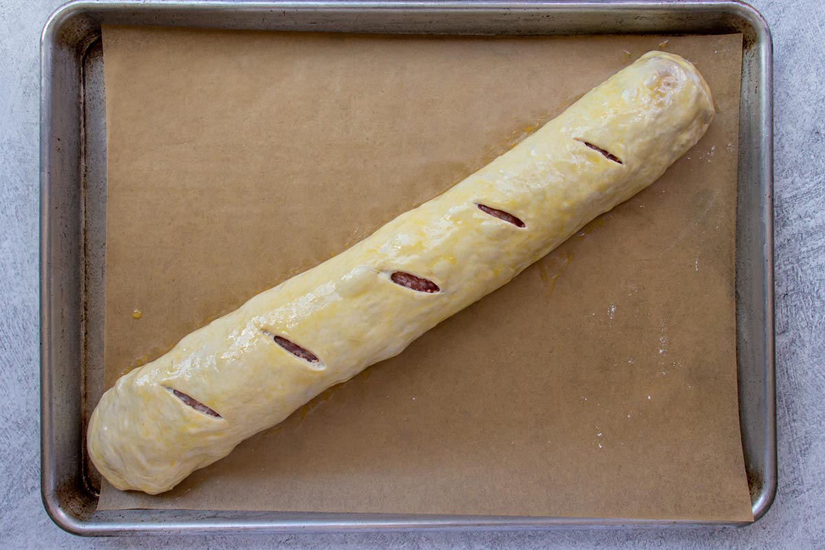 A roll of dough with five slits cut on top arranged diagonally on a baking sheet.