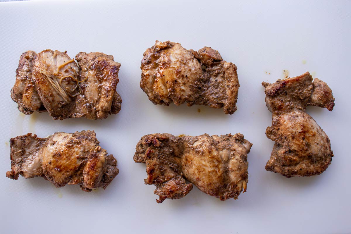 Cooked chicken shawarma thighs on a white cutting board.