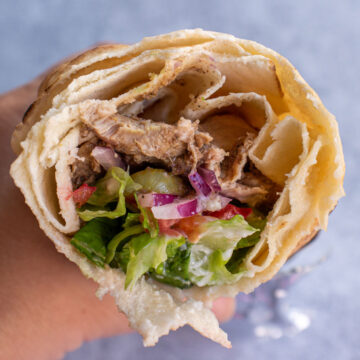 Closeup of the cross-section of a half-eaten hand-held chicken shawarma sandwich.