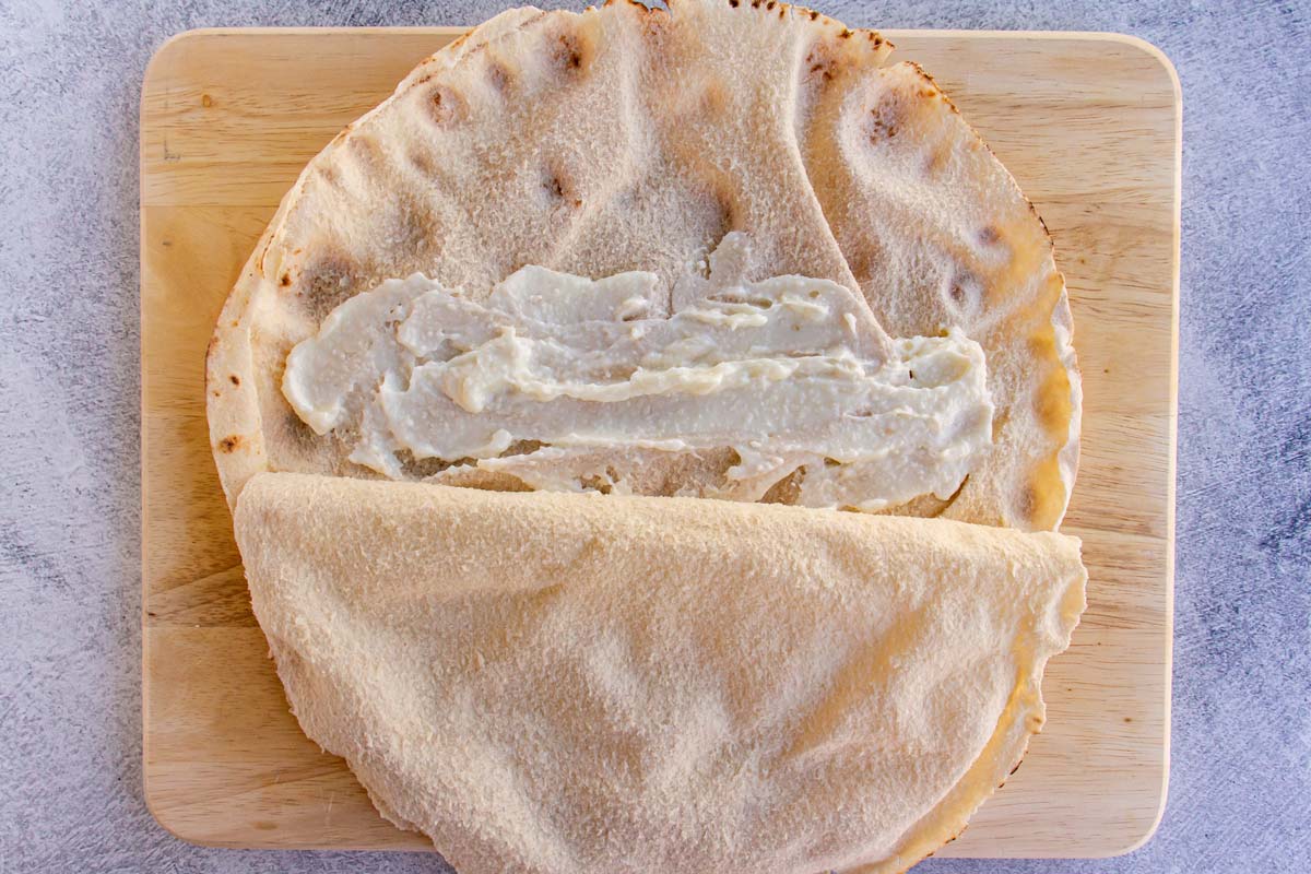 Thick white sauce spread inside a pita flatbread which has been opened halfway.