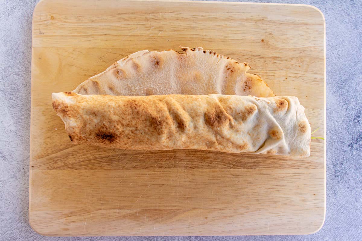 A partially rolled up pita wrap on a wooden board.
