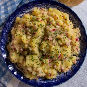 Austrian potato salad topped with chopped chives in a dark blue bowl.
