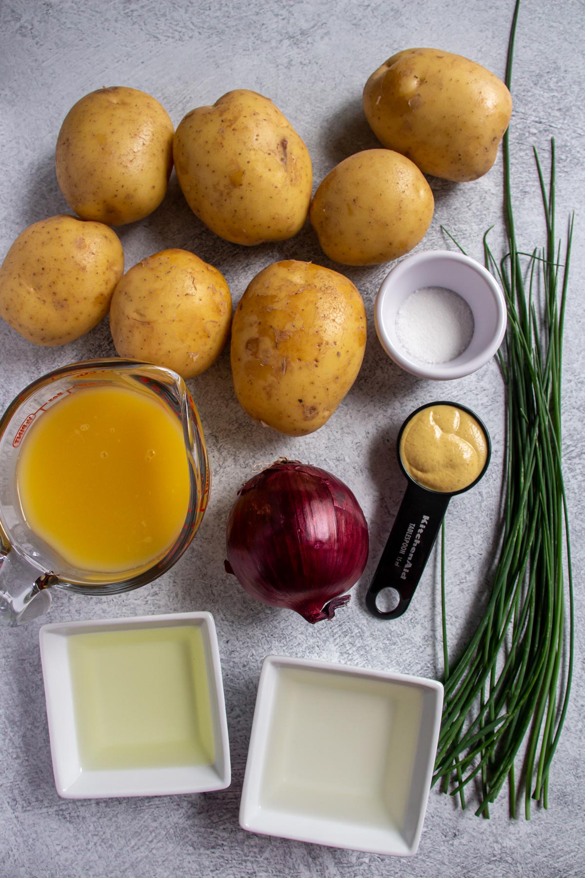 Ingredients for Austrian potato salad on a light grey background.