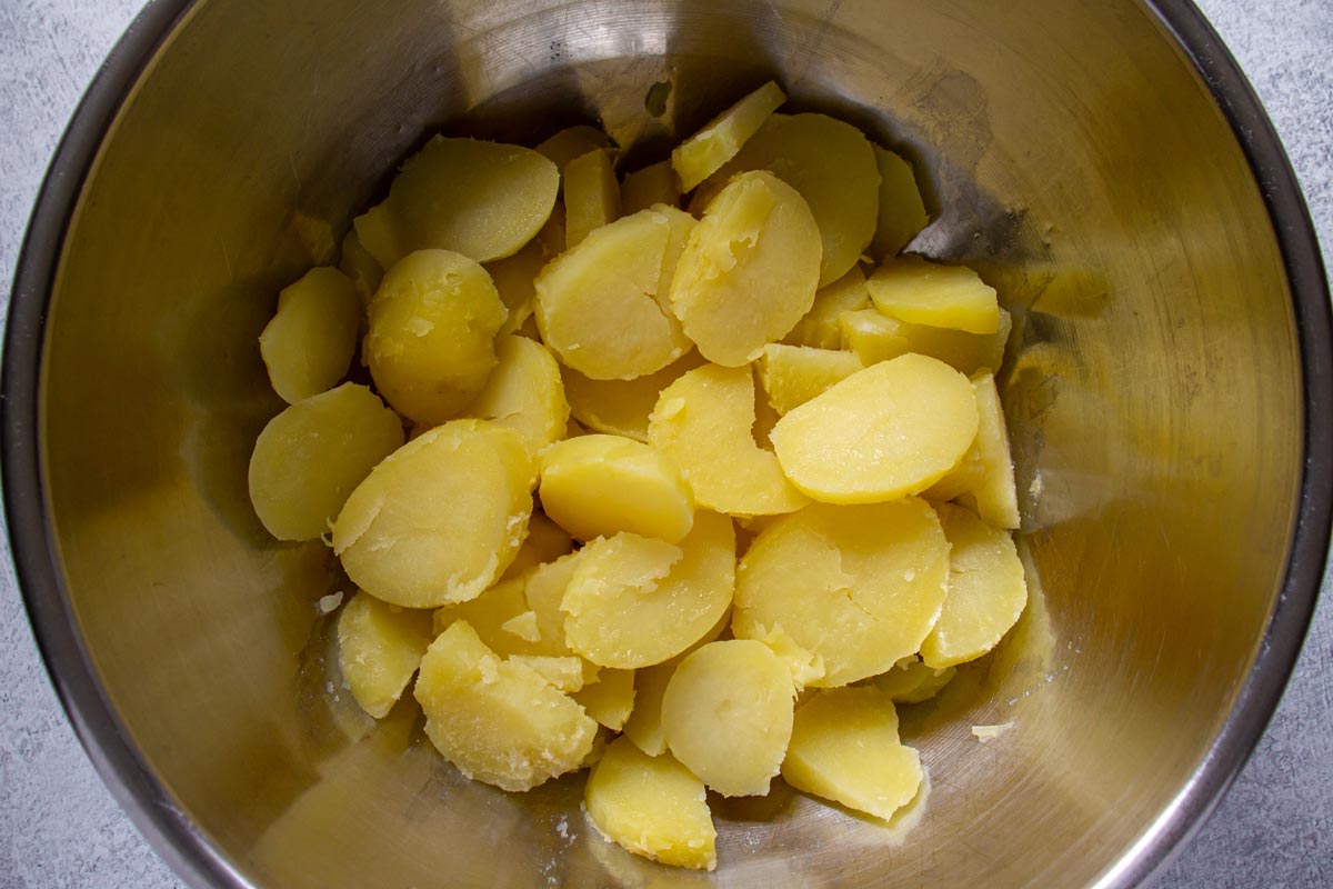 Sliced cooked potatoes in a metal mixing bowl.