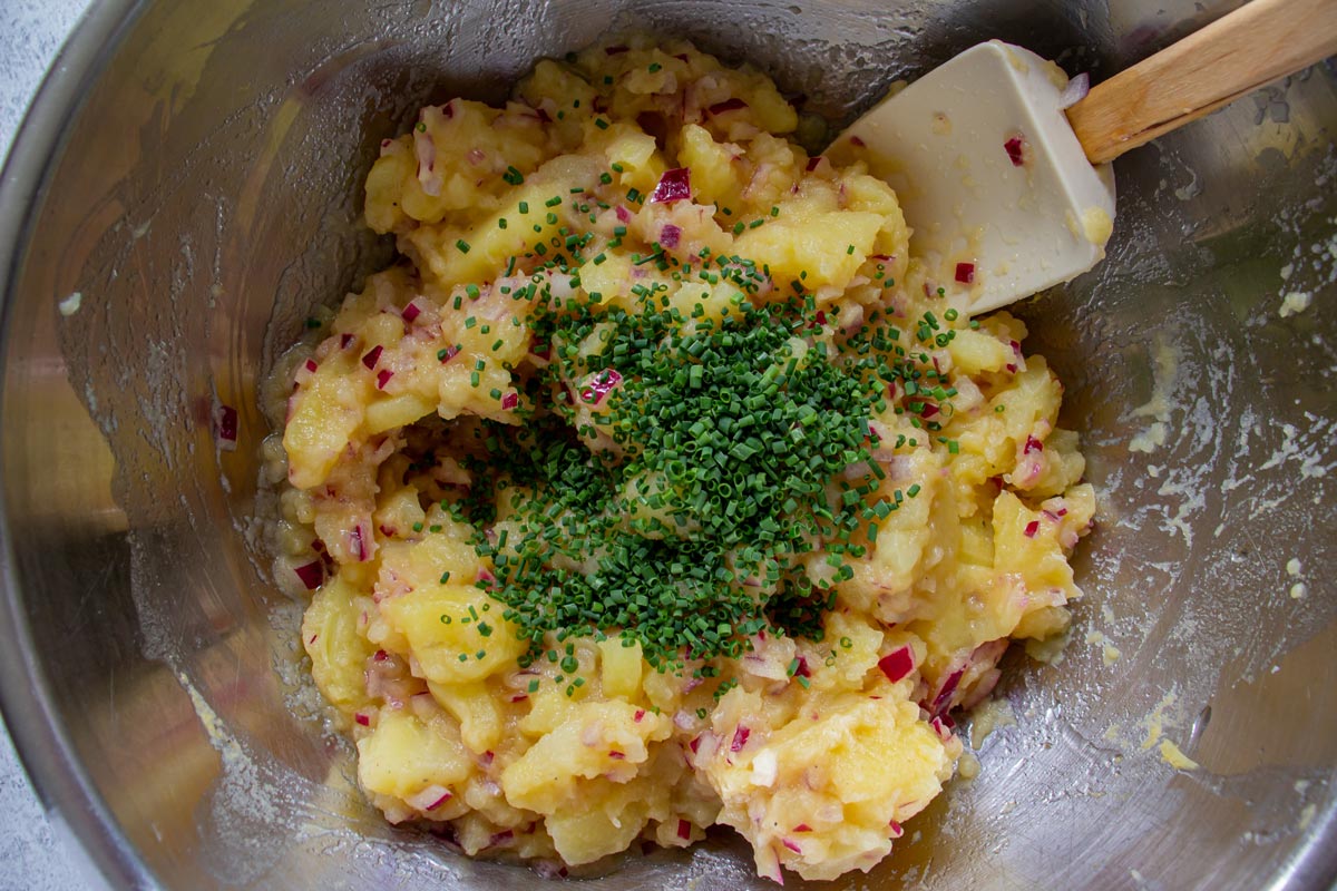 Potato salad topped with chopped chives in a metal mixing bowl.