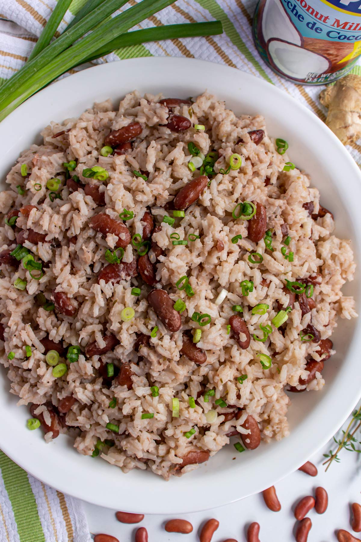 A bowl of rice and peas, scallions, dried kidney beans, and a can of coconut milk.