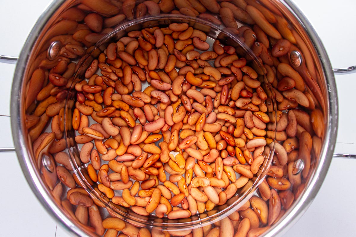 Red kidney beans covered with water in a metal pot.