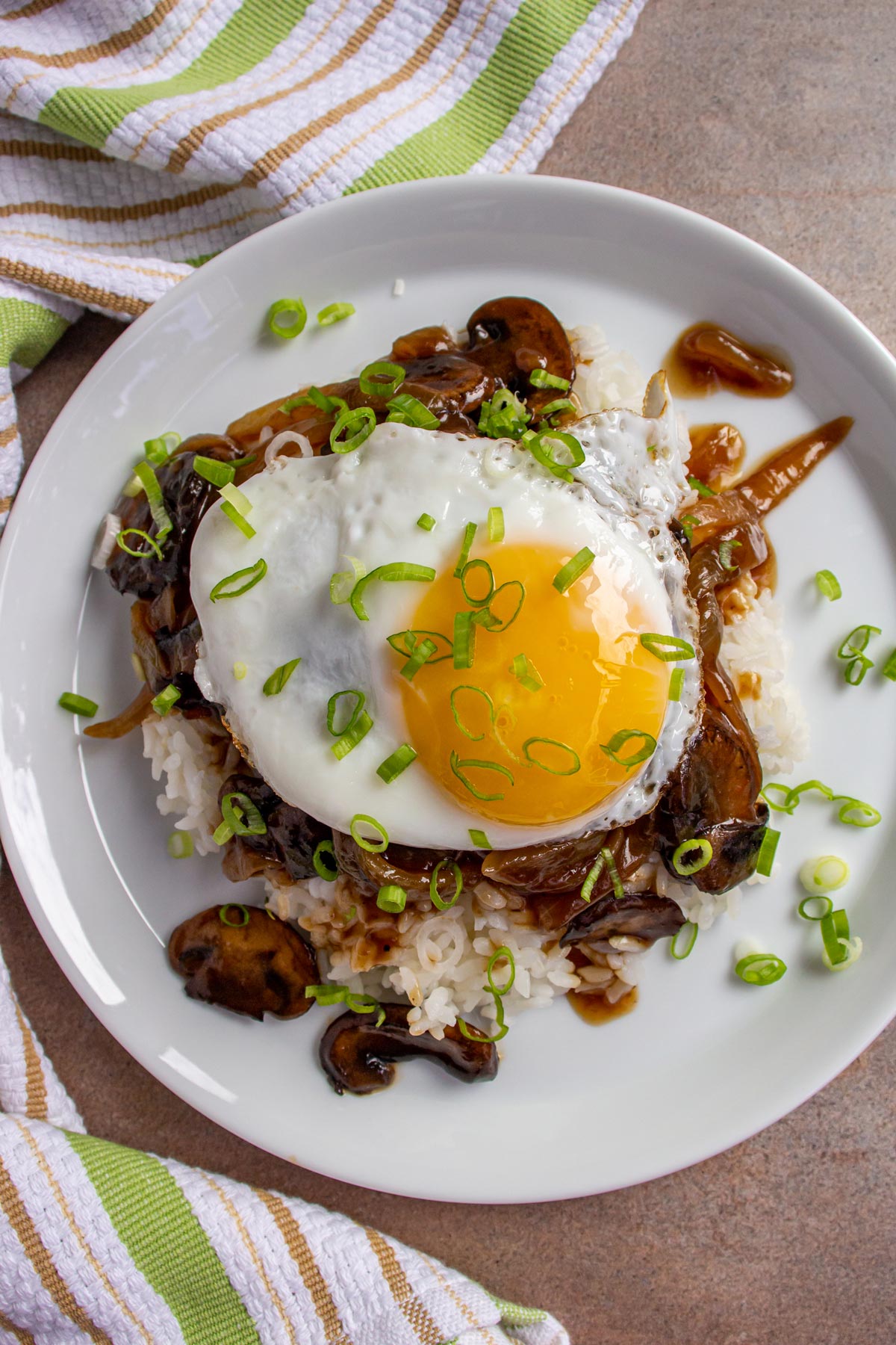 A fried egg on top of a plate of white rice and dark brown gravy.