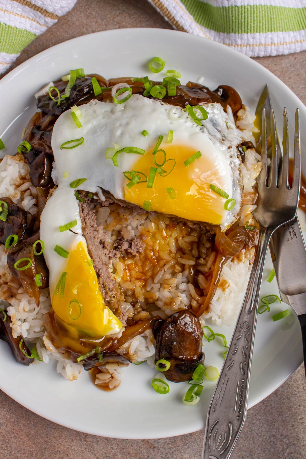 A loco moco on a white plate cut to reveal the burger patty and runny yolk.