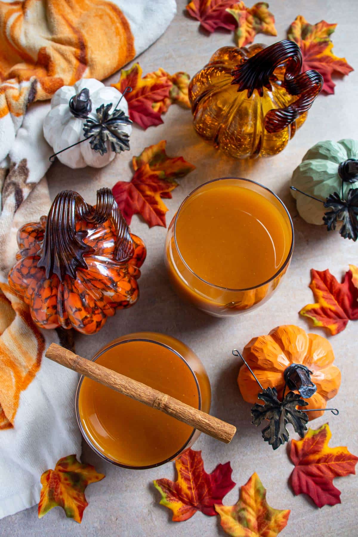 Two glasses of pumpkin juice surrounded by fake autumn leaves and pumpkins.