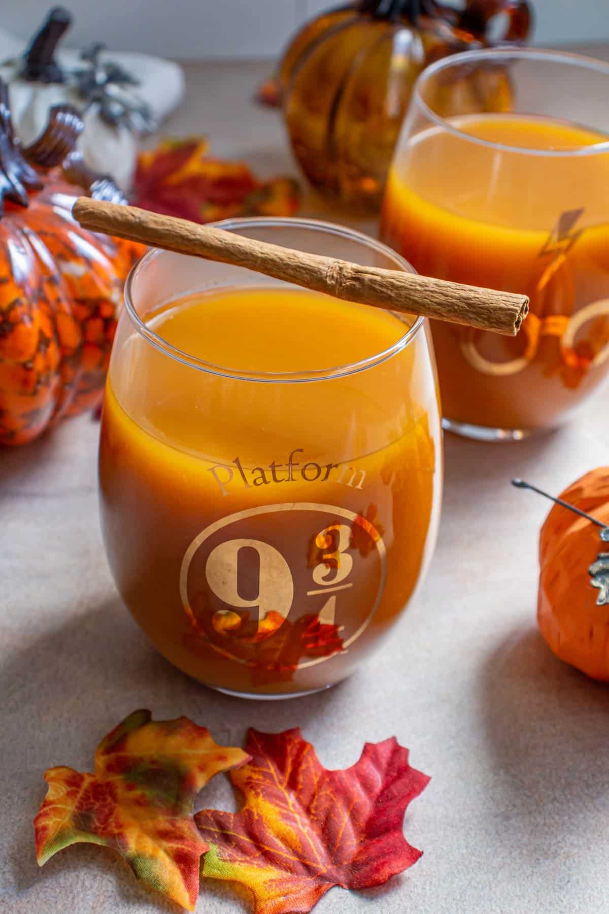Two glasses of pumpkin juice, one with a cinnamon stick resting on top of it.