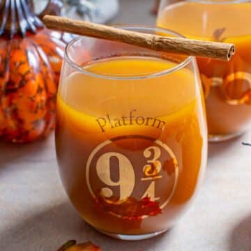 An orange colored drink in a glass that says platform nine and three-quarters on it.