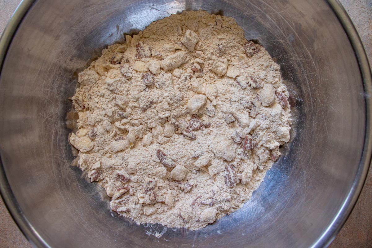 A dry mixture with chopped pecans in a metal mixing bowl.
