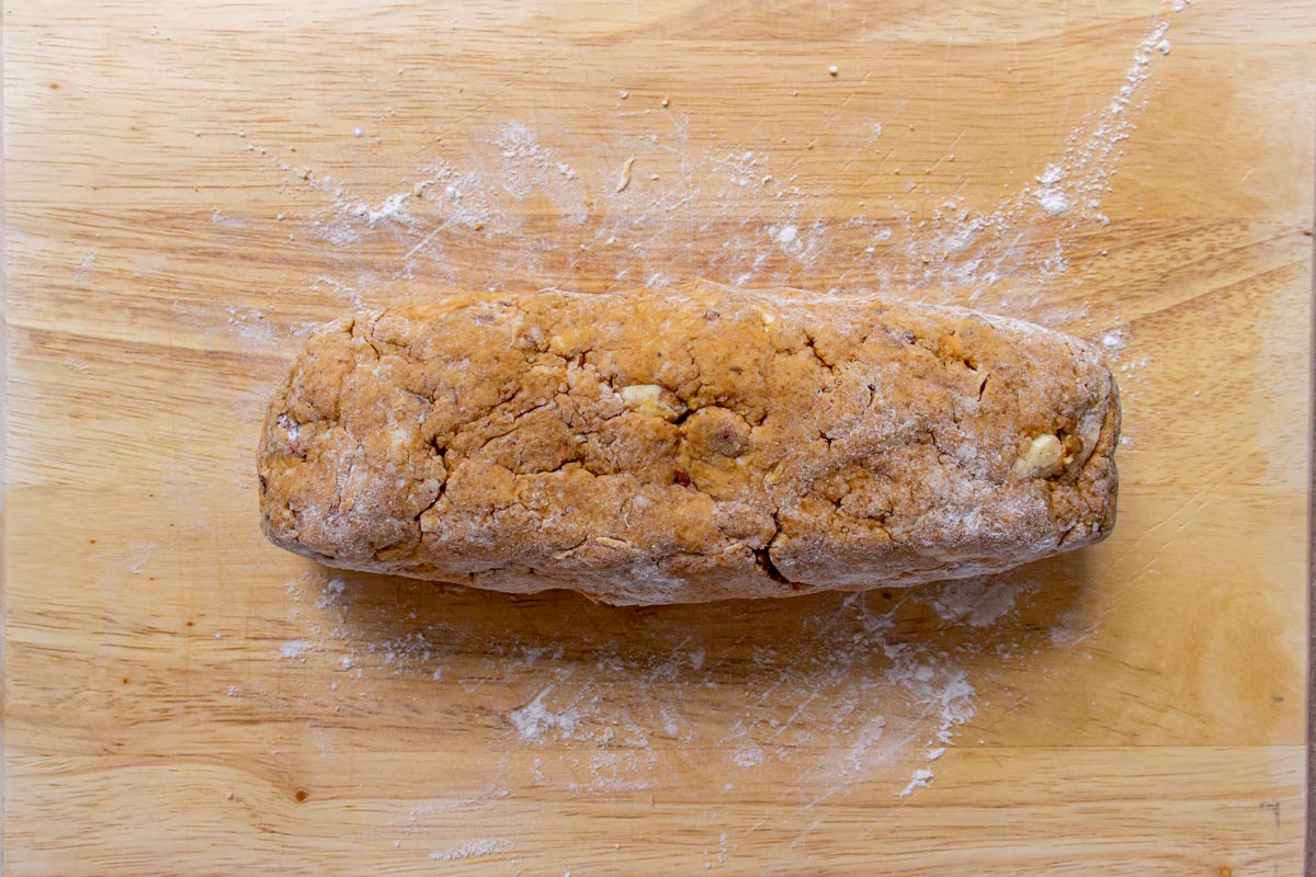 A short log of dough on a floured wooden work surface.
