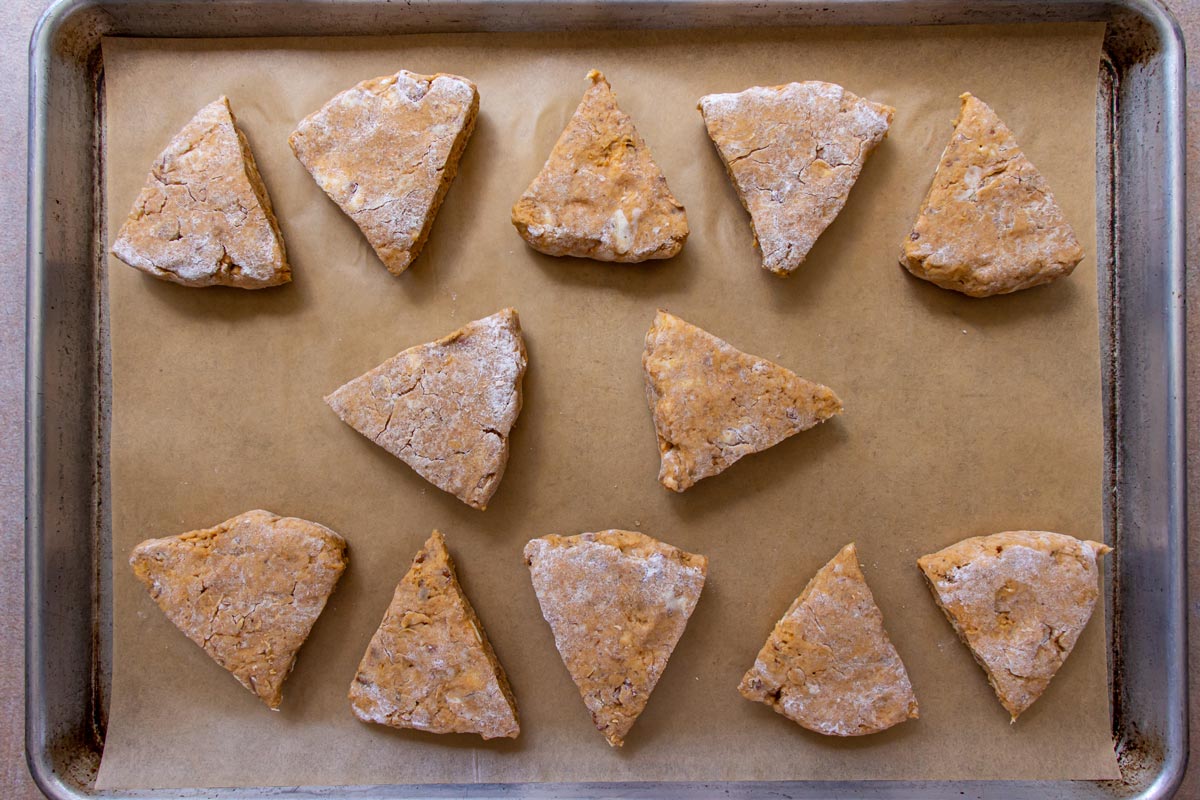 Unbaked triangles of pumpkin scone dough on a parchment paper lined baking sheet.