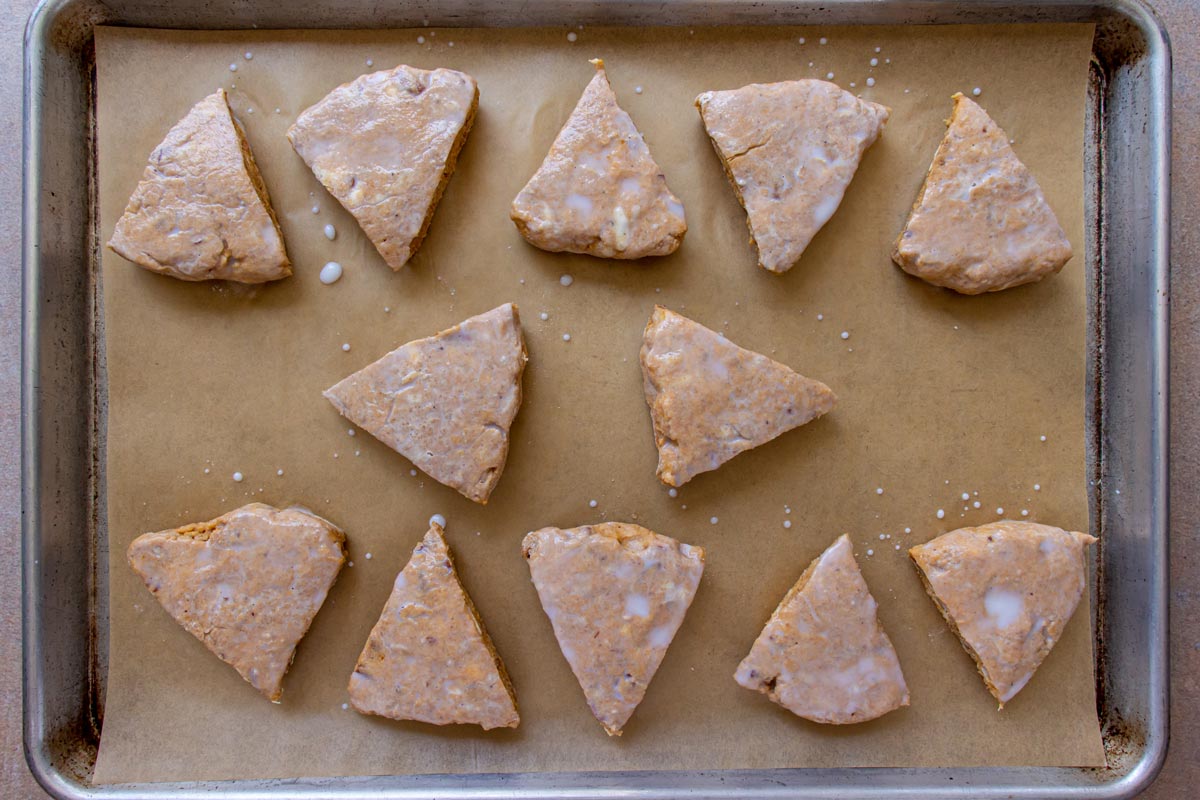 Wedges of pumpkin scone dough on a parchment paper lined baking sheet brushed with milk.