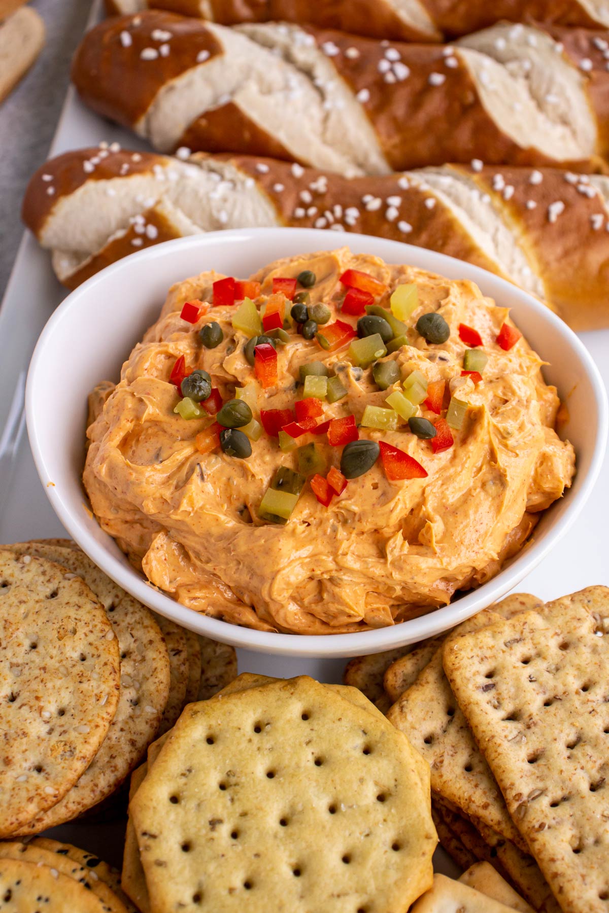 Liptauer cheese spread in a white bowl surrounded by crackers and soft pretzels sticks.