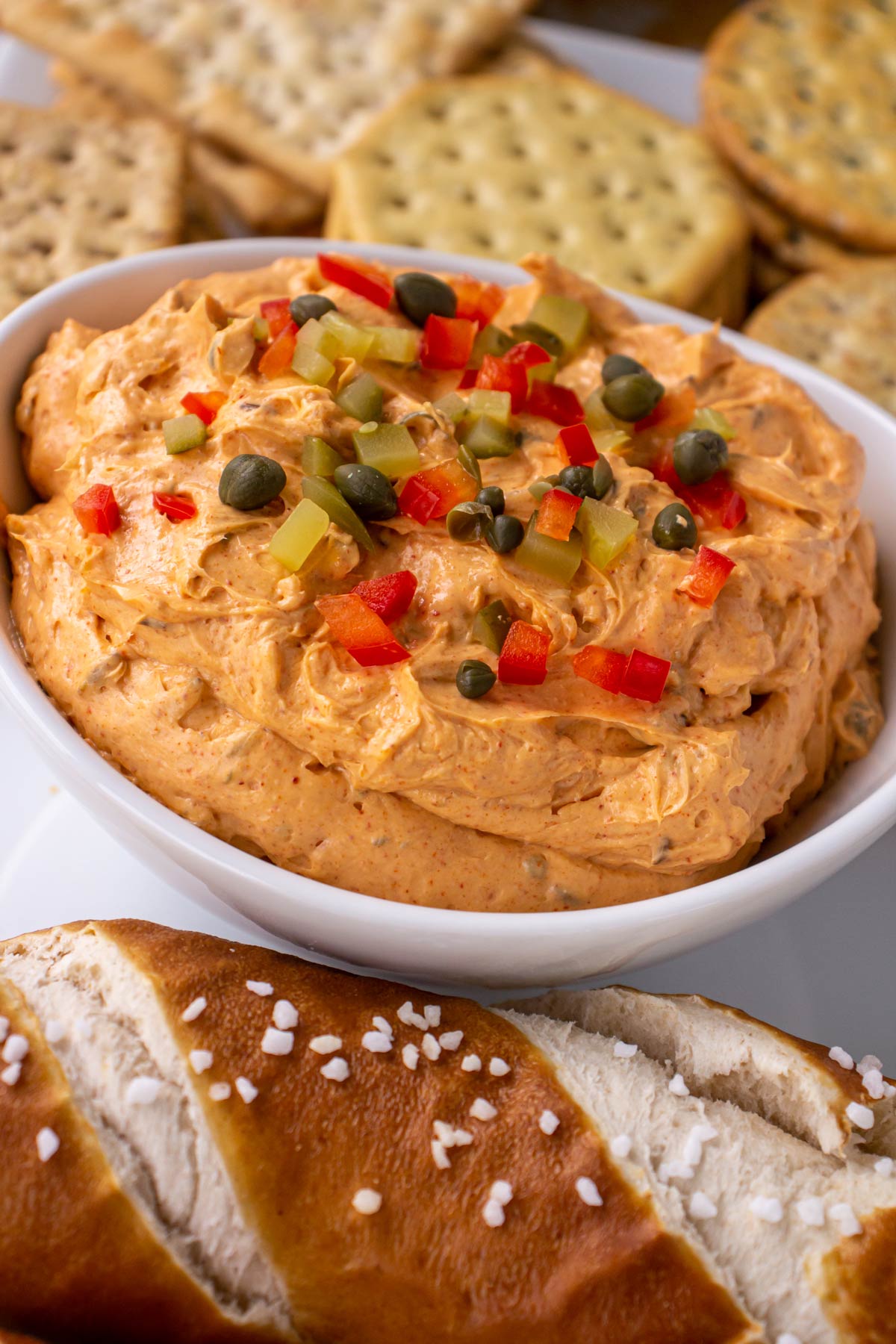 Closeup of Liptauer cheese spread topped with red peppers and capers surrounded by pretzels and crackers.