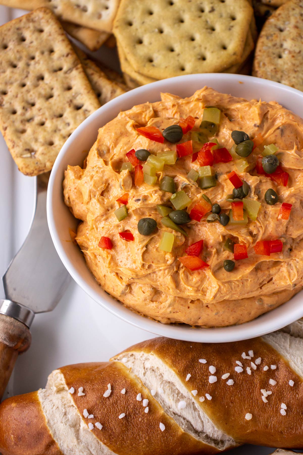 A bowl of paprika-infused cheese spread with crackers and soft pretzels on either side.
