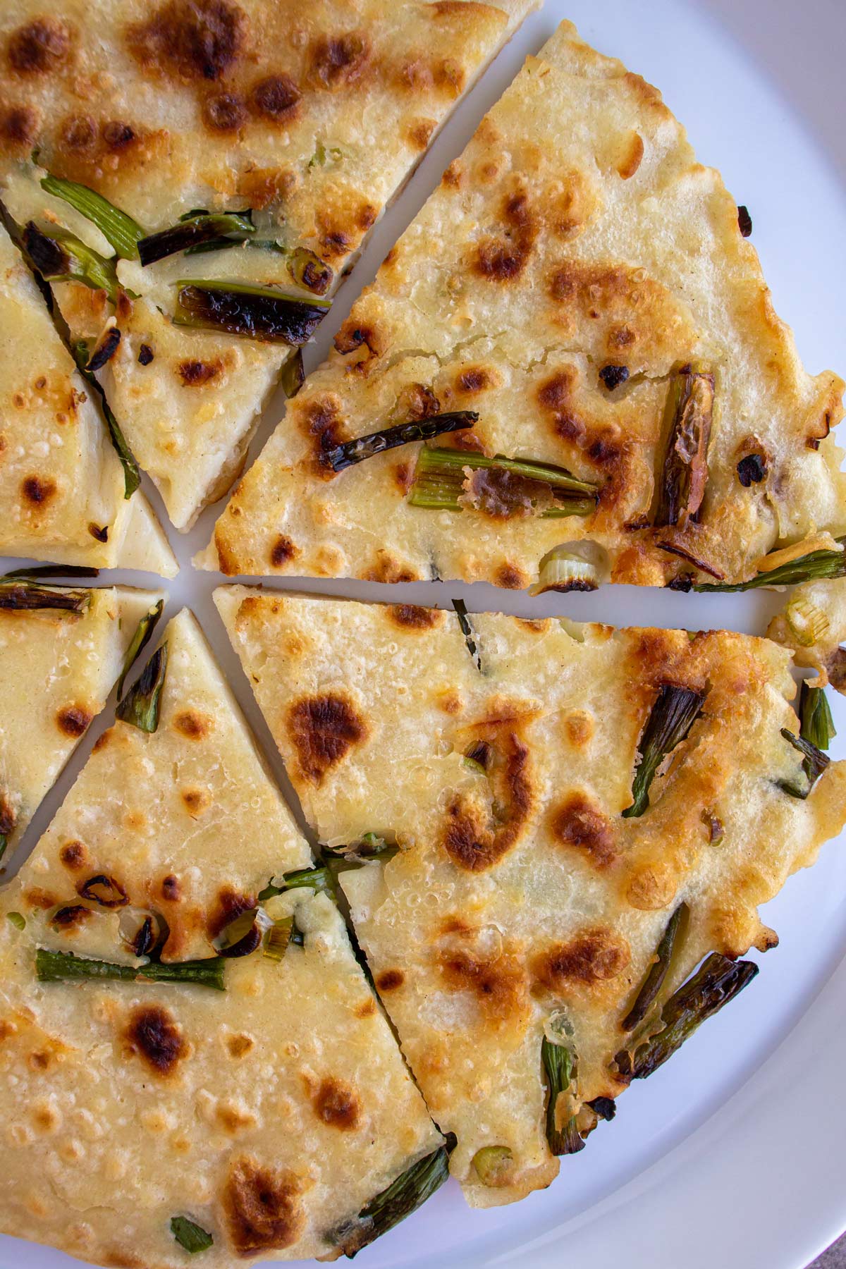 Closeup of a scallion pancake cut into 6 wedges on a white plate.