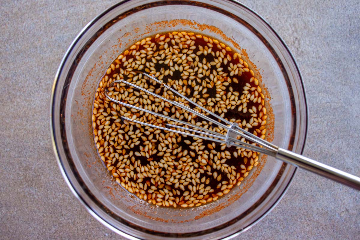 Korean dipping sauce with sesame seeds in a small glass bowl with a little whisk.