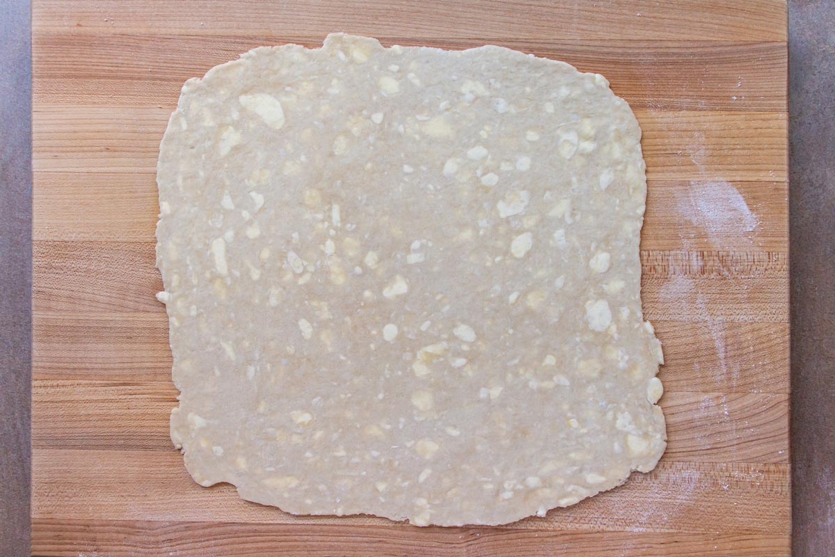 Homemade pie dough rolled into a square shape on a wooden board.