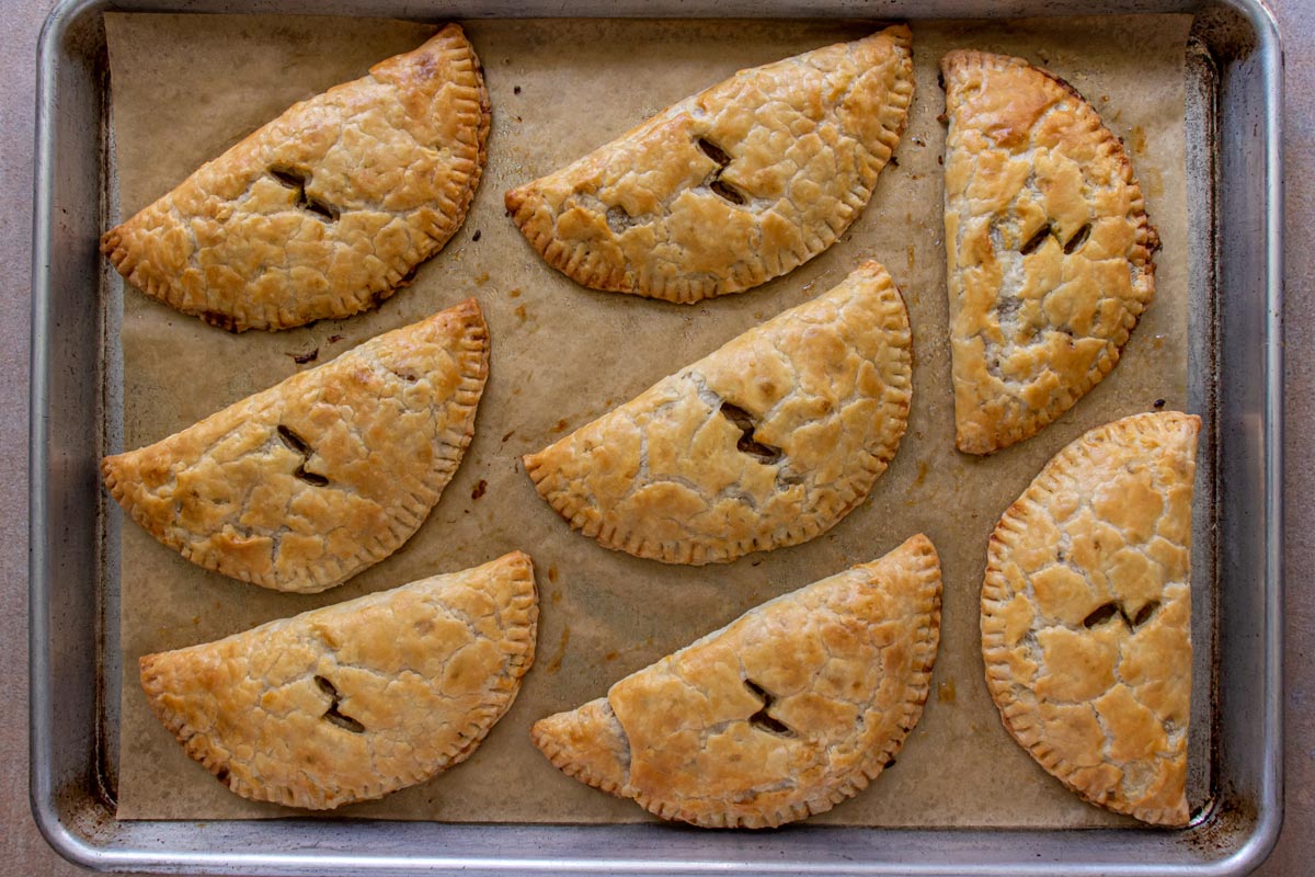 Eight baked pumpkin pasties on a parchment paper lined sheet pan.