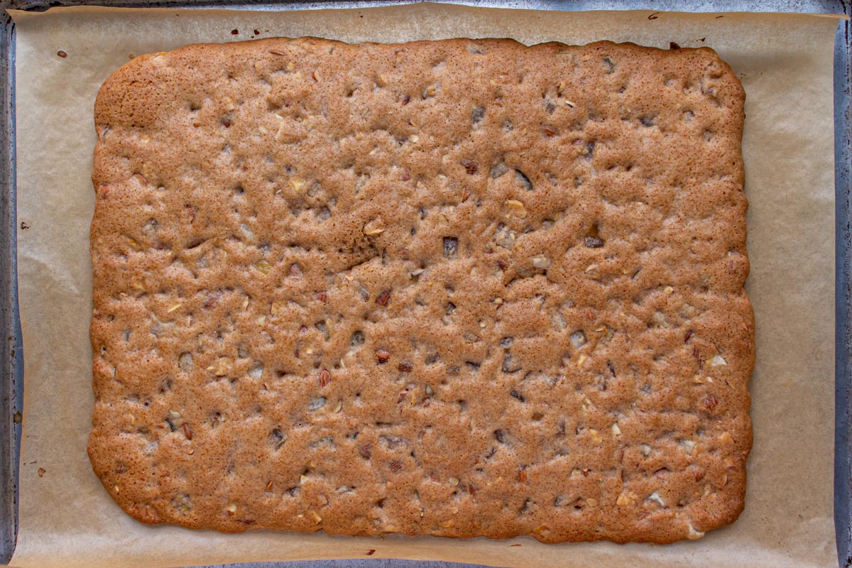A baked rectangle of leckerli dough on a parchment paper lined sheet pan.