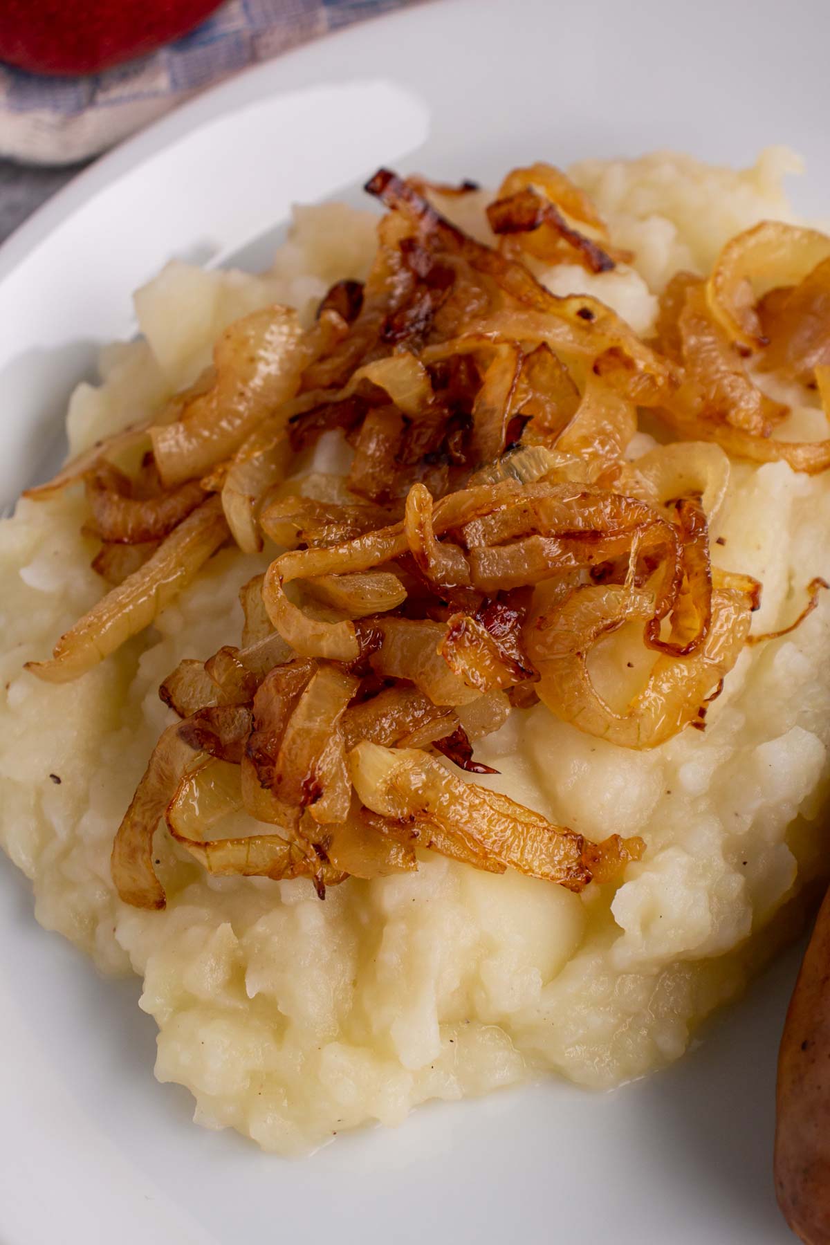 Closeup of mashed potatoes with apples topped with fried onions on a white plate.