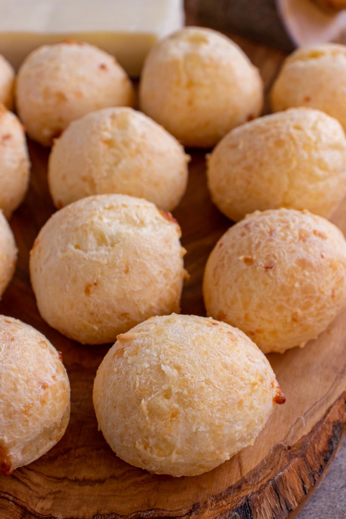 Closeup of small spherical Brazilian cheese breads arranged on a wooden board.