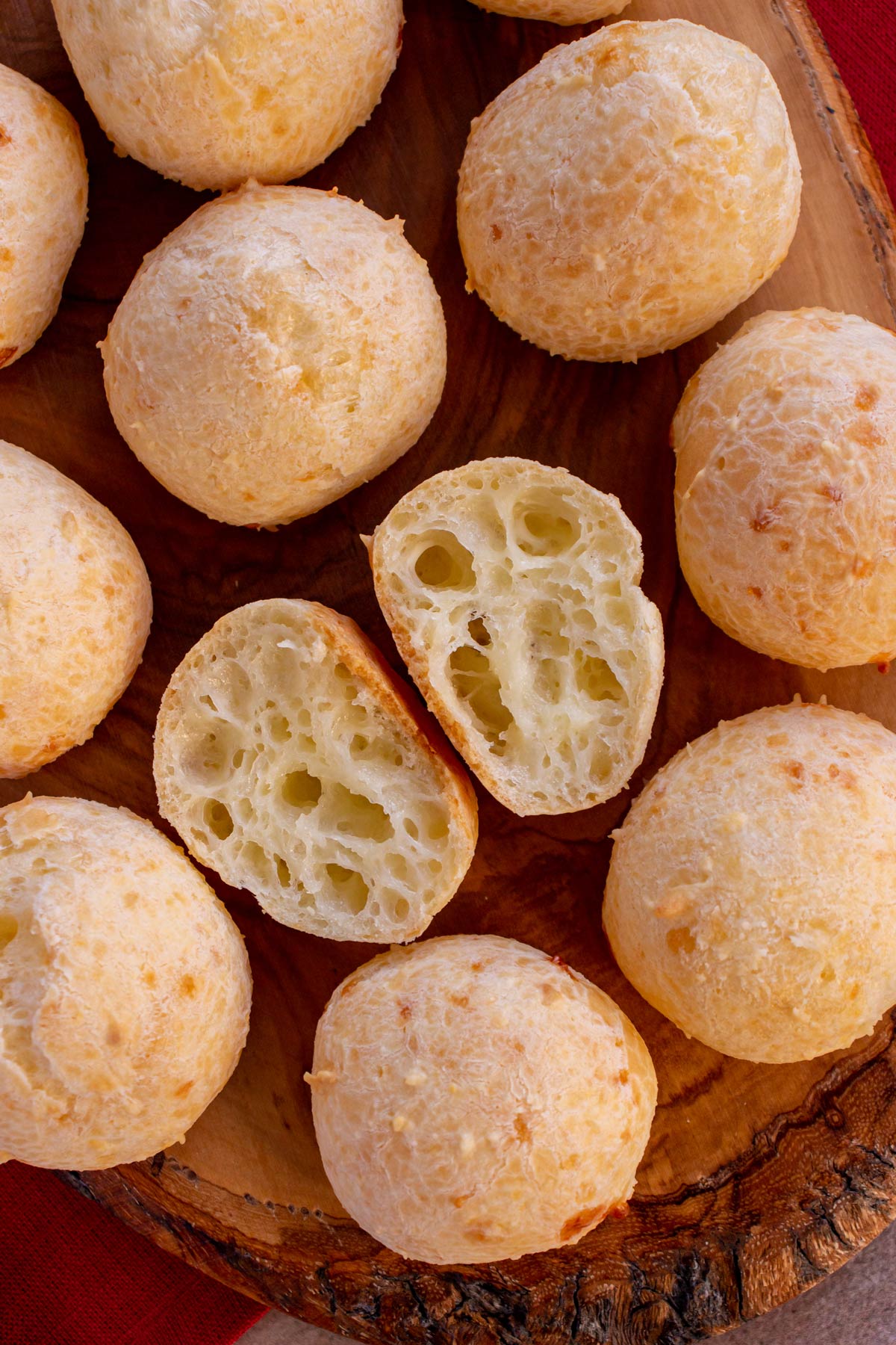 Round lightly golden Brazilian cheese breads on a wooden surface with one cut in half.