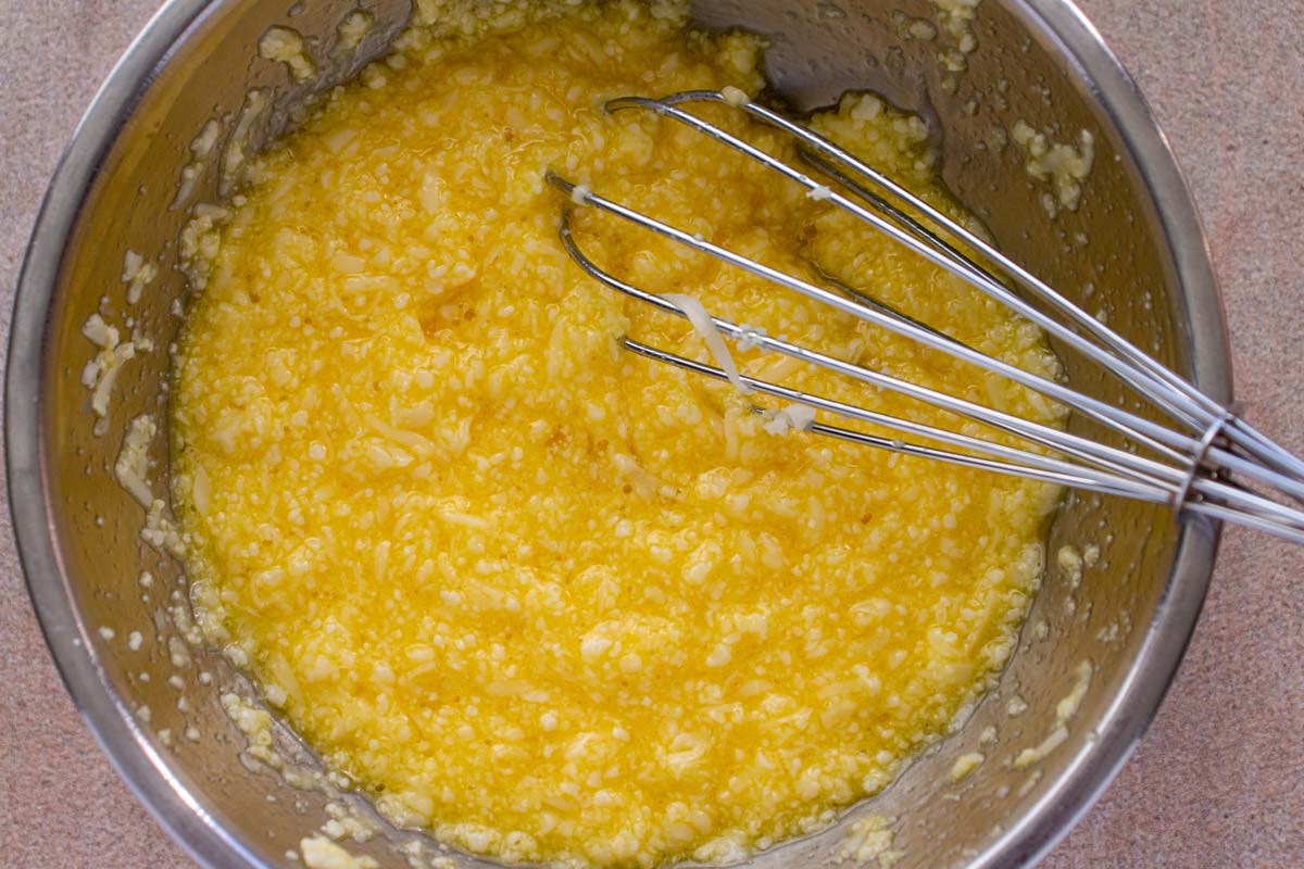 Eggs beaten together with finely grated cheese with a small whisk in a metal bowl.