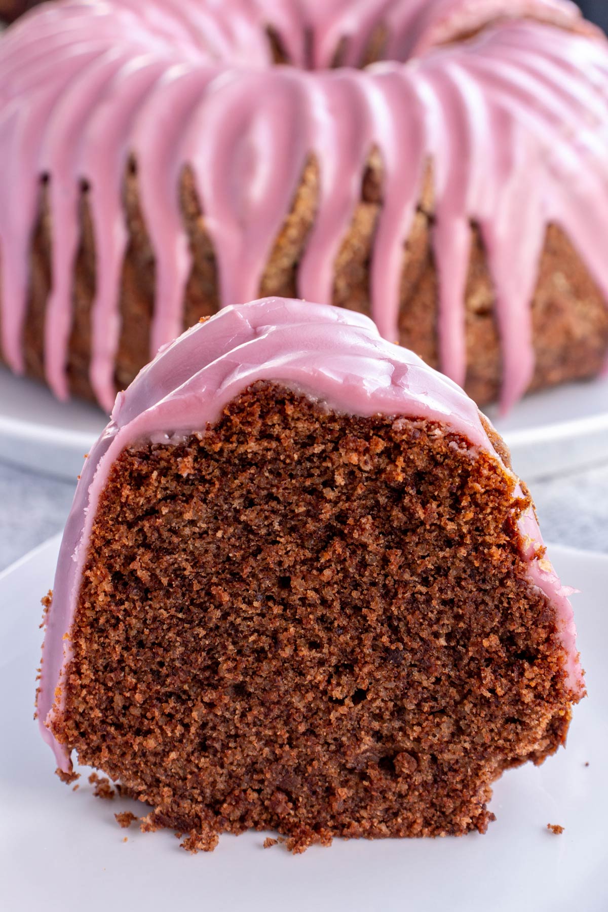 A slice of chocolate Bundt cake with red wine glaze with the whole cake behind it.