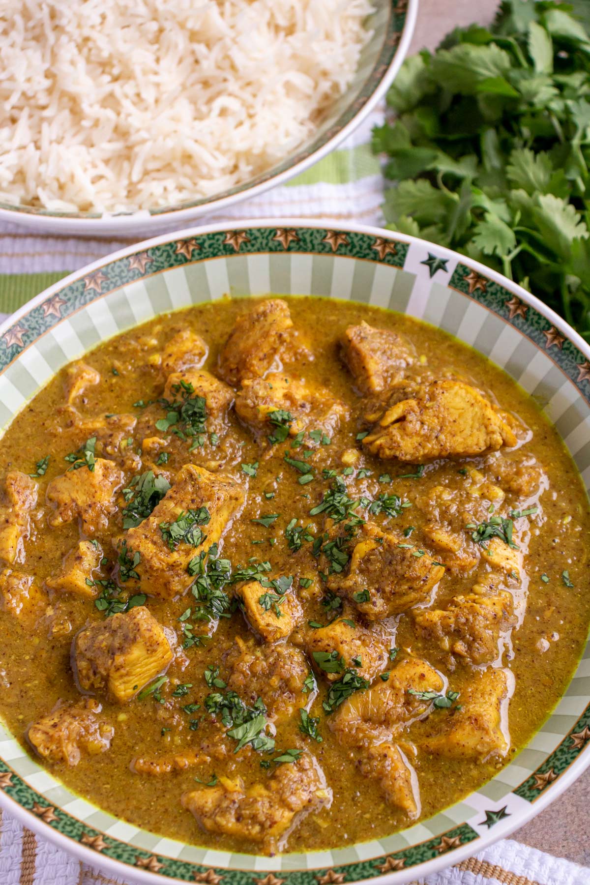 A green and white bowl filled with chicken vindaloo curry with white rice in the background.