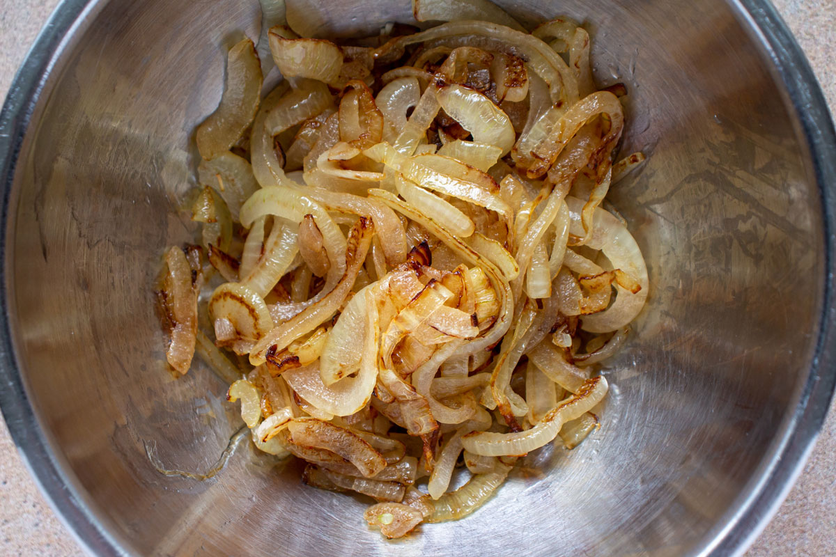 Lightly browned cooked sliced onions in a metal bowl.