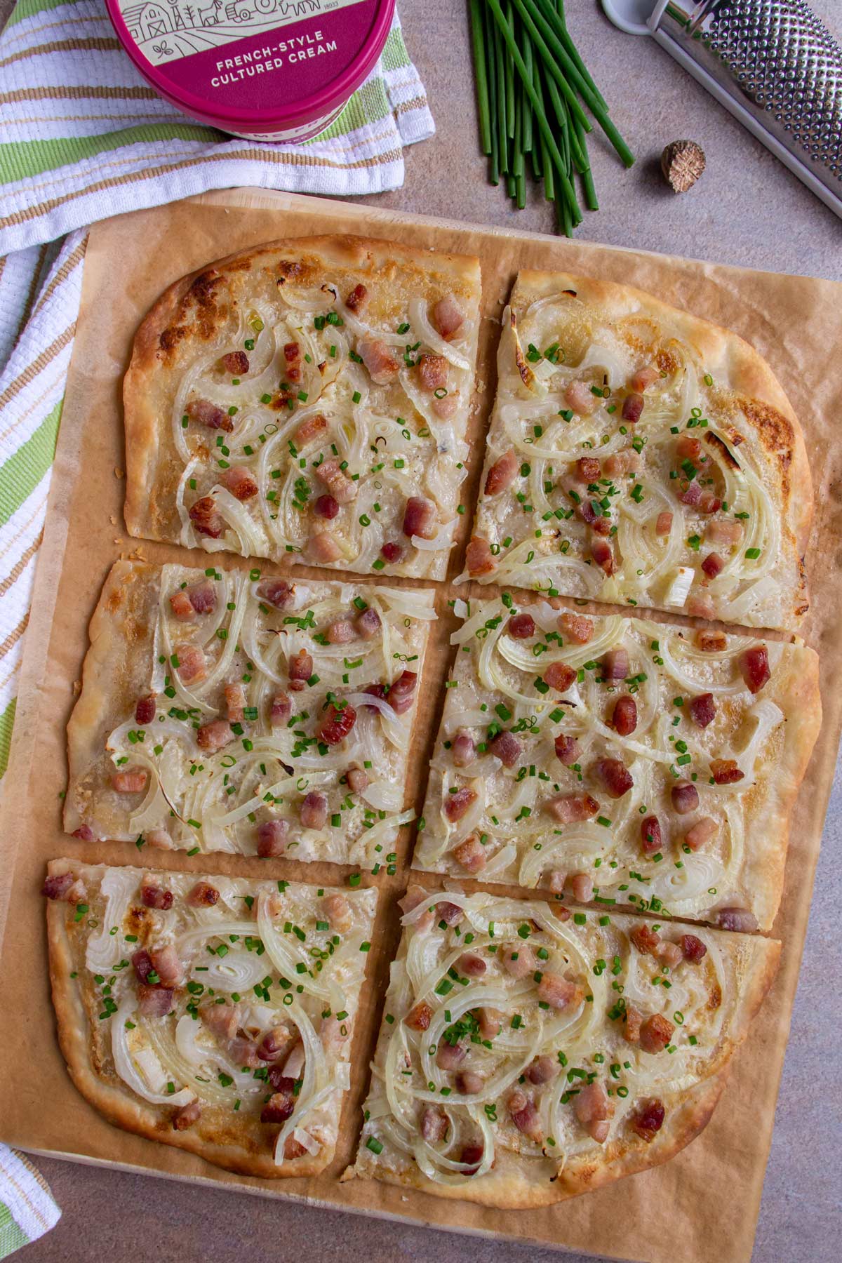 Six square pieces of flammkuchen German bacon and onion flatbread pizza with chives on brown parchment.
