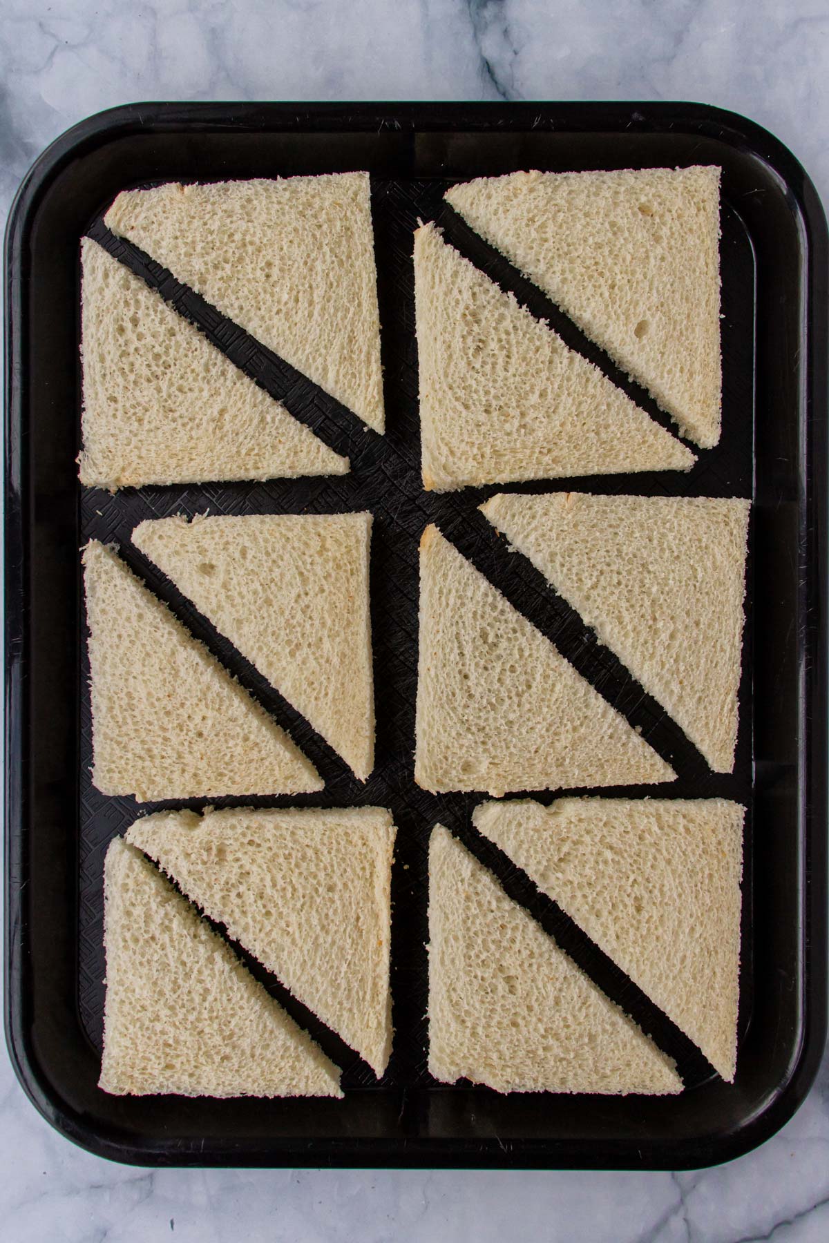 Six slices of white bread with crusts removed, cut in half diagonally on a black tray.
