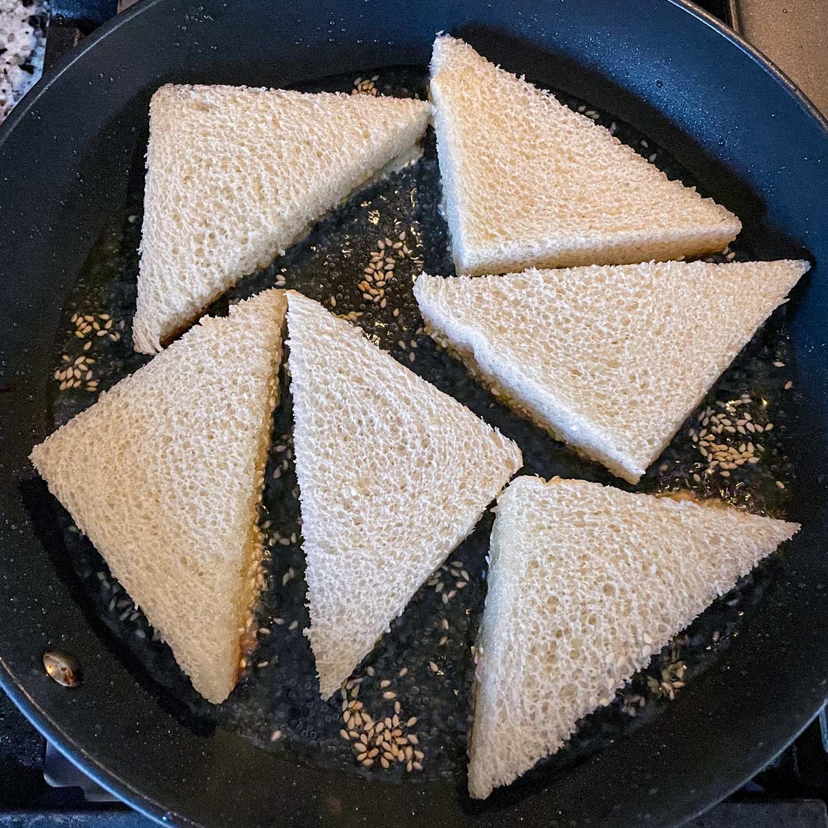 Six triangular pieces of bread shallow frying in a nonstick skillet.