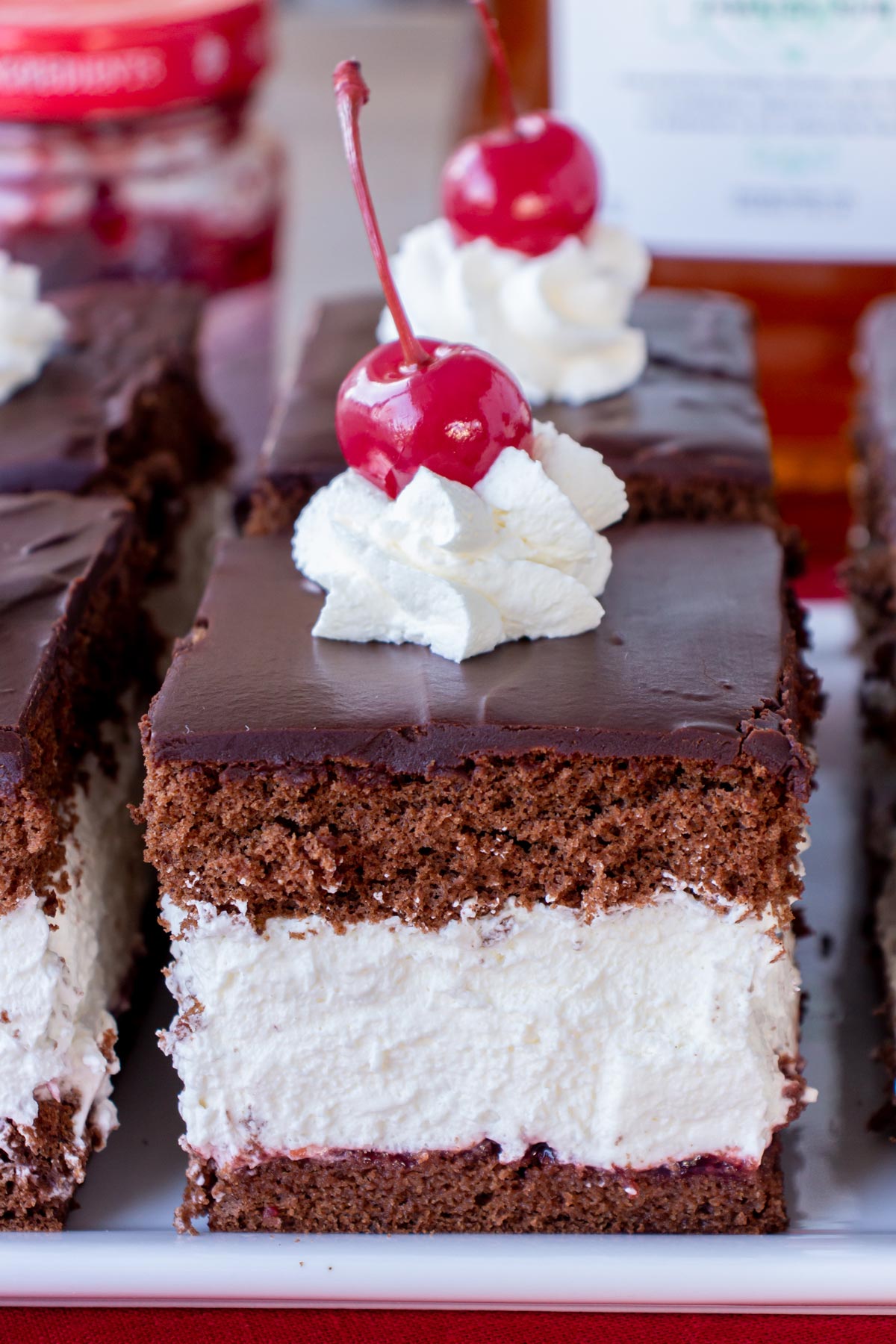 Closeup of Wuzetka chocolate cream cake squares topped with whipped cream rosettes and cherries.