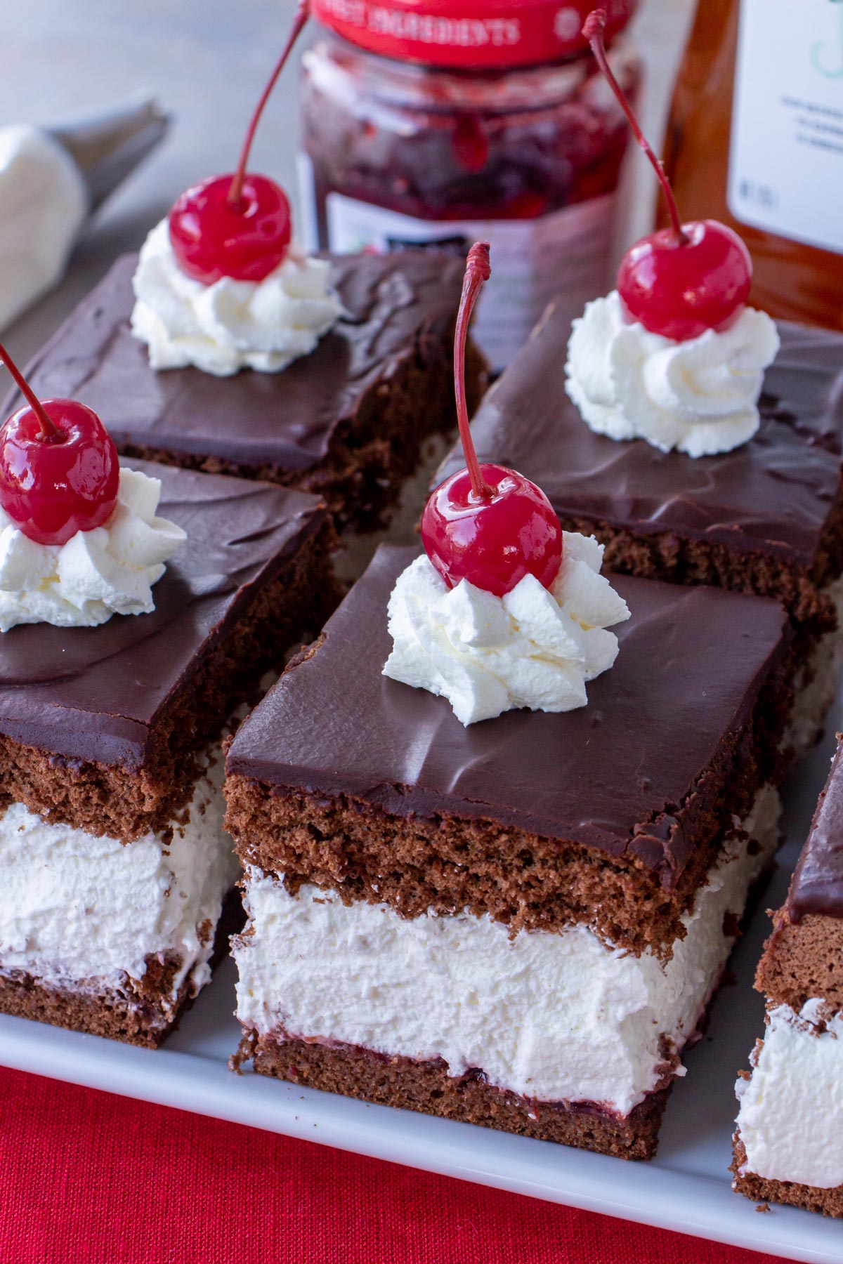 Square pieces of chocolate cake filled with thick whipped cream and topped with cherries.