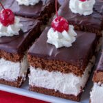 Closeup of Wuzetka chocolate cream cake squares topped with whipped cream rosettes and cherries.