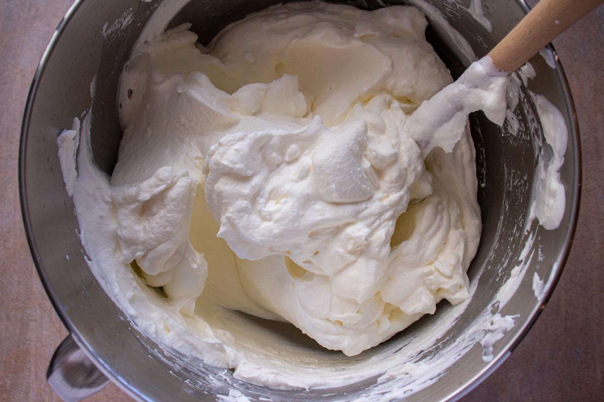 Thick homemade whipped cream with a rubber spatula in a metal mixing bowl.
