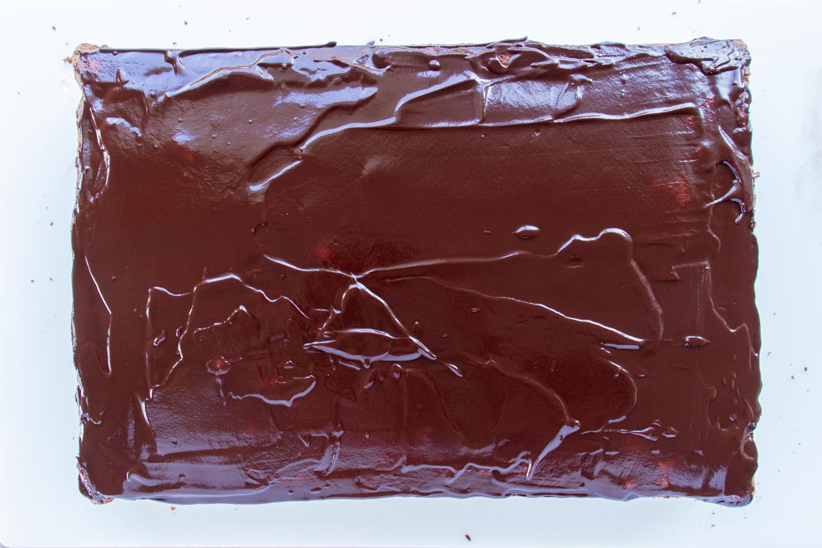 Chocolate ganache spread in a thin layer over a rectangular cake.