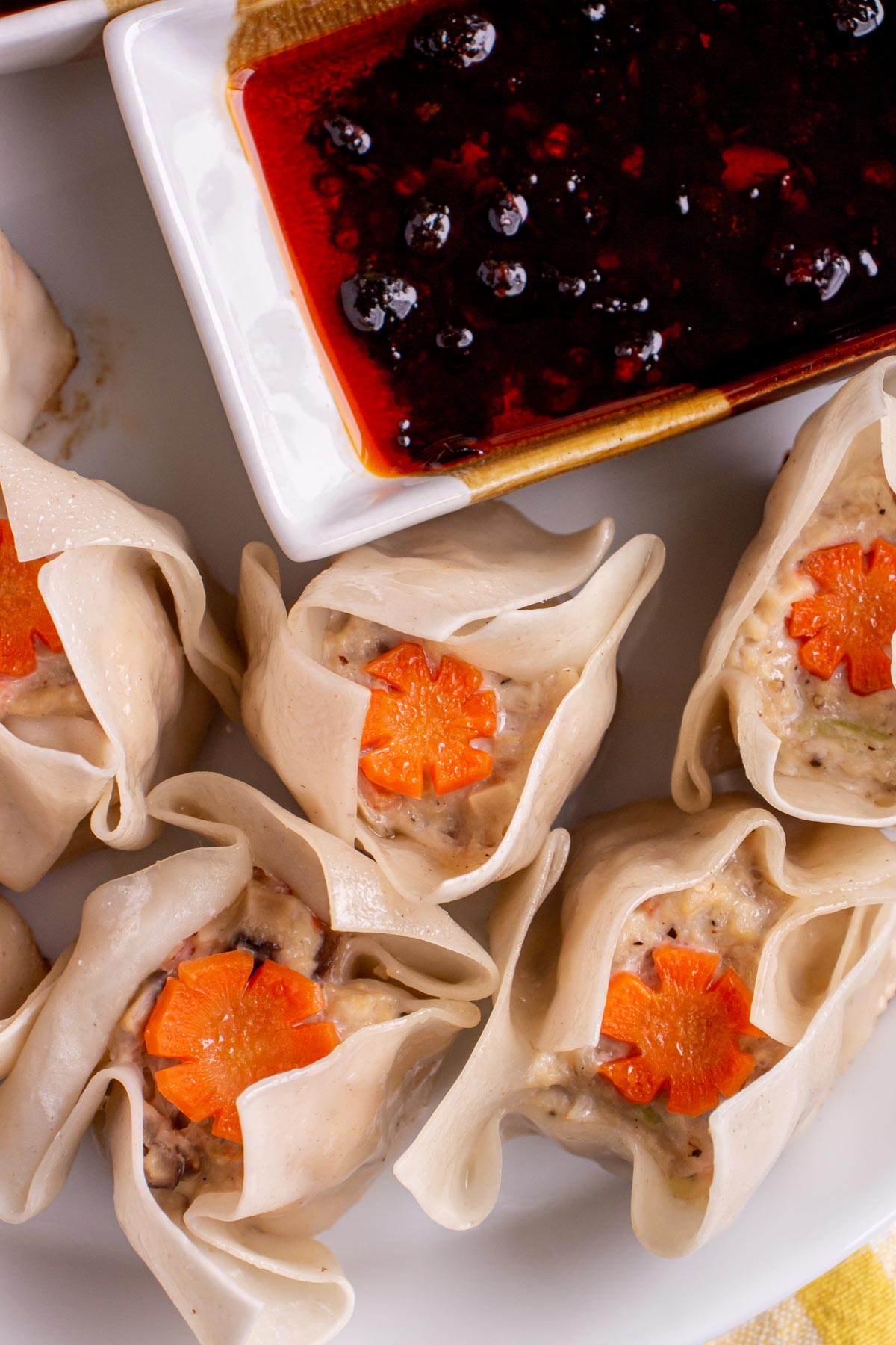 Closeup of chicken siu mai dumplings with decorative carrot garnish and a side of chili oil.