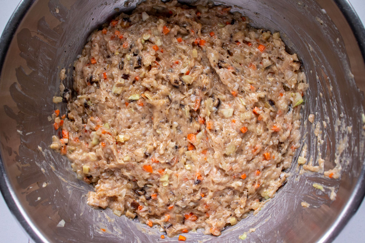 A ground chicken mixture with finely chopped vegetables in a metal mixing bowl.