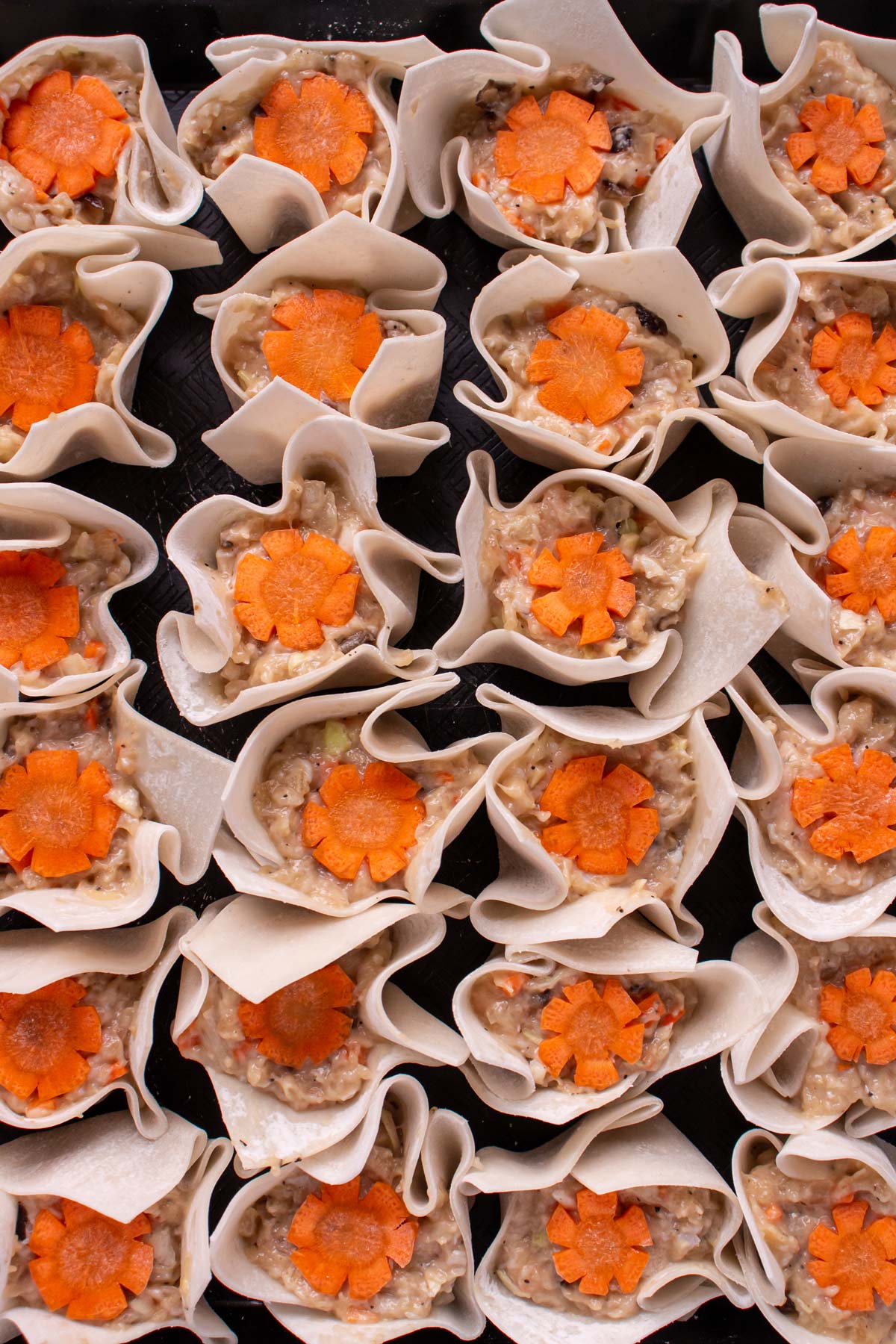 Rows of open-faced chicken siu mai dumplings garnished with decoratively cut carrots.
